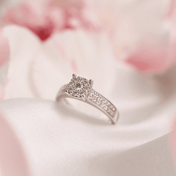 En glitrende diamantforlovelsesring med dekorert ringbånd hviler på mykt rosa og hvitt satengstoff.