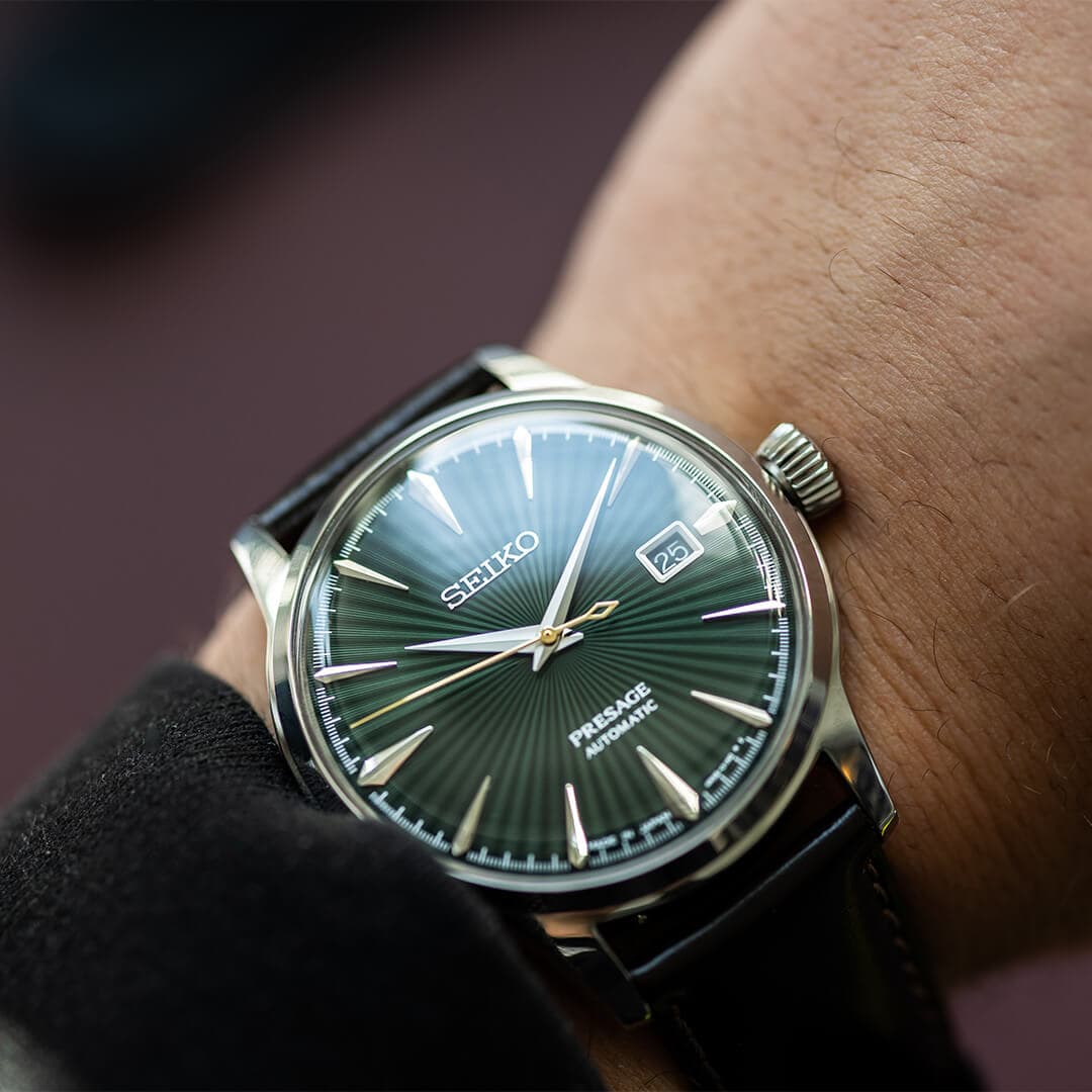 Håndledd med en Seiko Presage-klokke. Grønn urskive med solstråle-effekt, sølvmarkører, datovisning og svart lærreim.