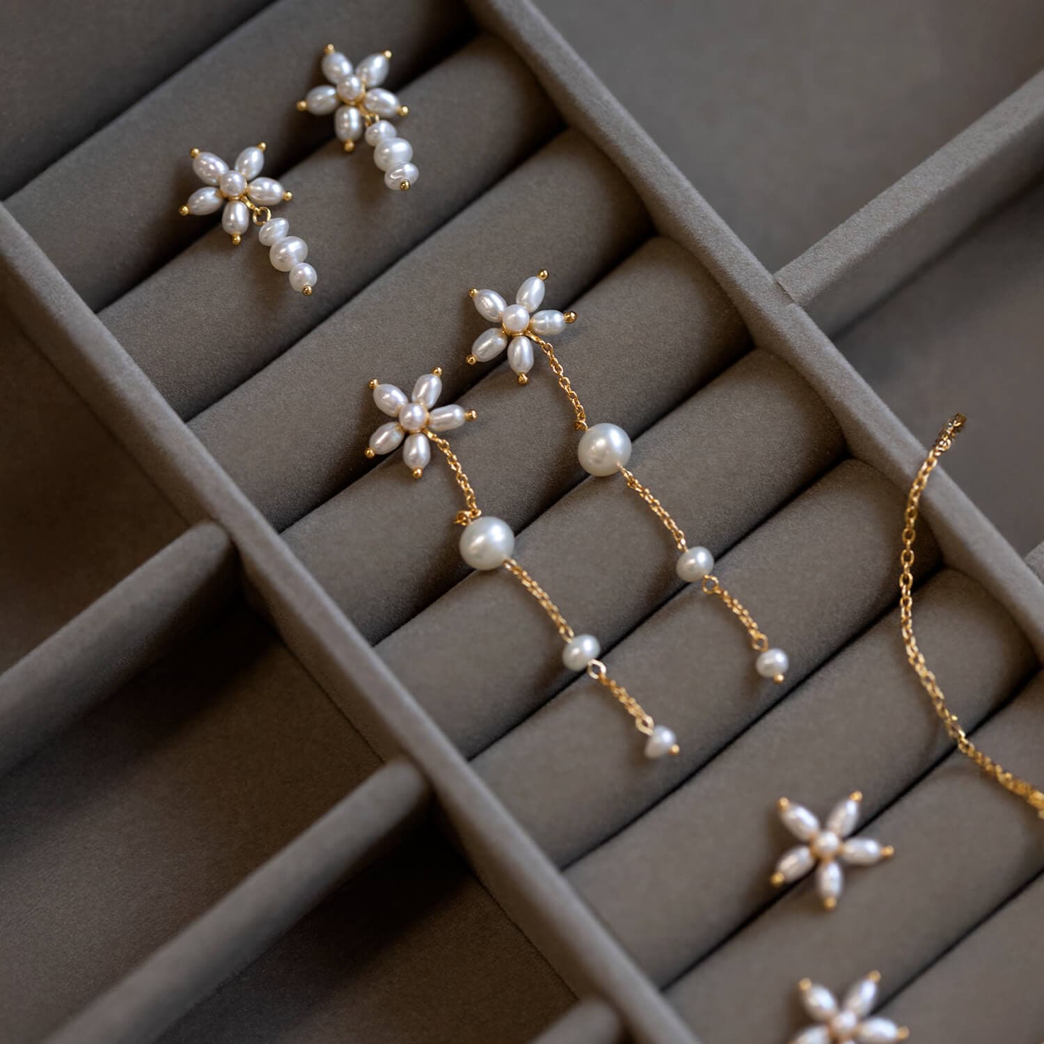 Gull- og perleøreringer med stjerne- og blomsterdesign vises i et foret smykkeskrin.